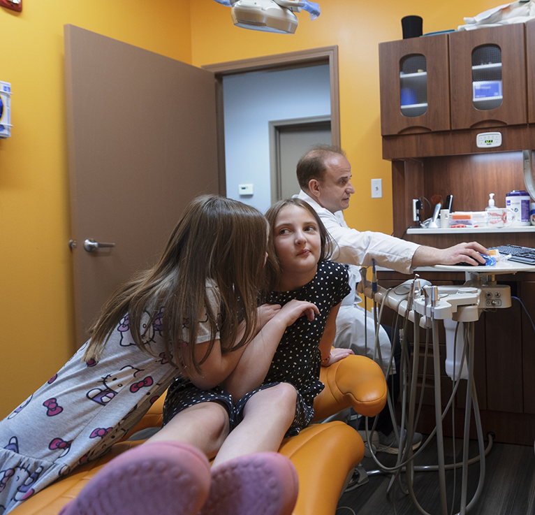 Little girl in dental chair talking to another little girl while waiting for dentist