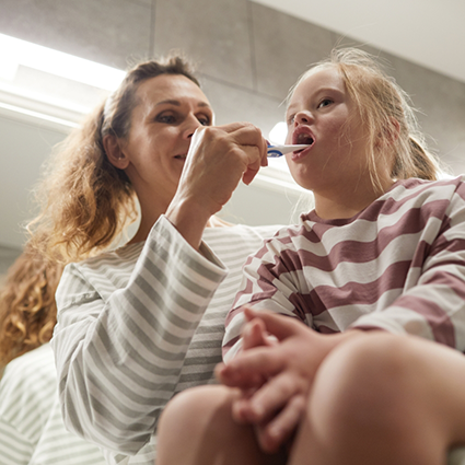 Little girl with striped sweater holding mouth open for female dentist
