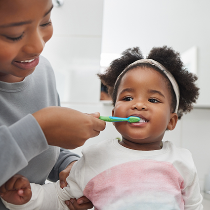 Little girl having teeth brushed by parent