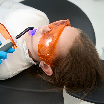 Little girl leaning back in dental chair having dental sealants placed