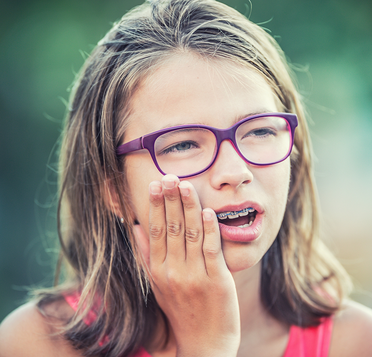 Little girl with glasses and braces rubbing jaw in pain