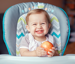 Infant in high chair holding an apple